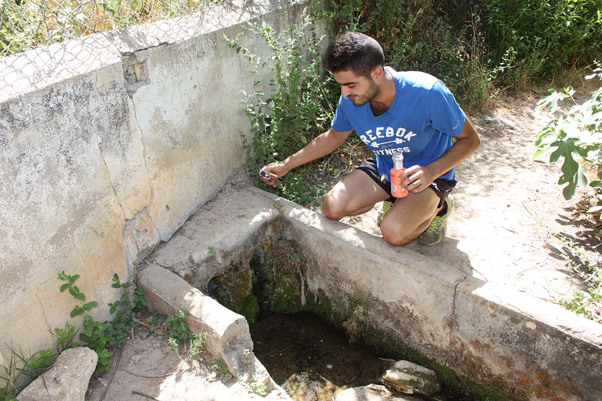 Un joven intenta llenar una botella en el nacimiento, que ofrece un bajo caudal.