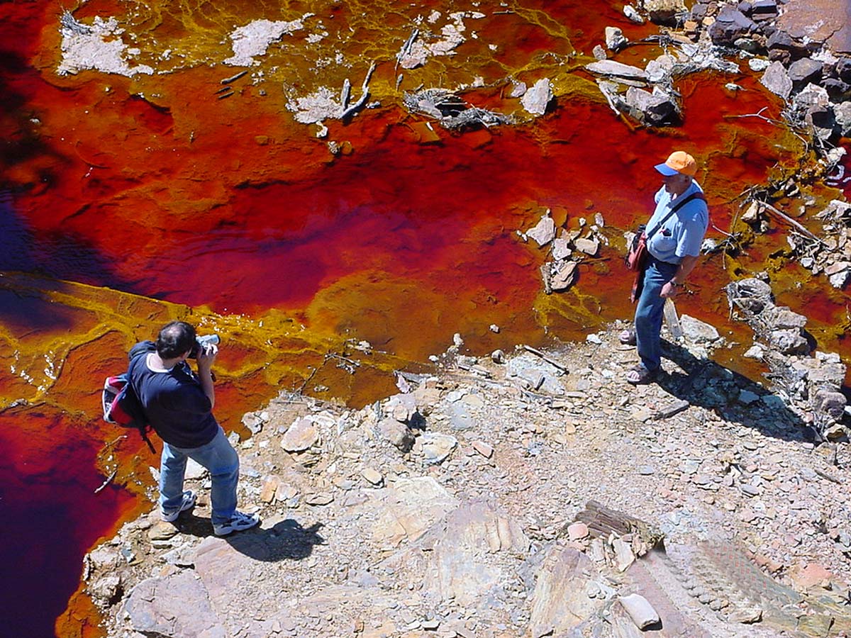 Dos componentes del grupo de excursionistas fotografiándose junto a las aguas rojas del río.