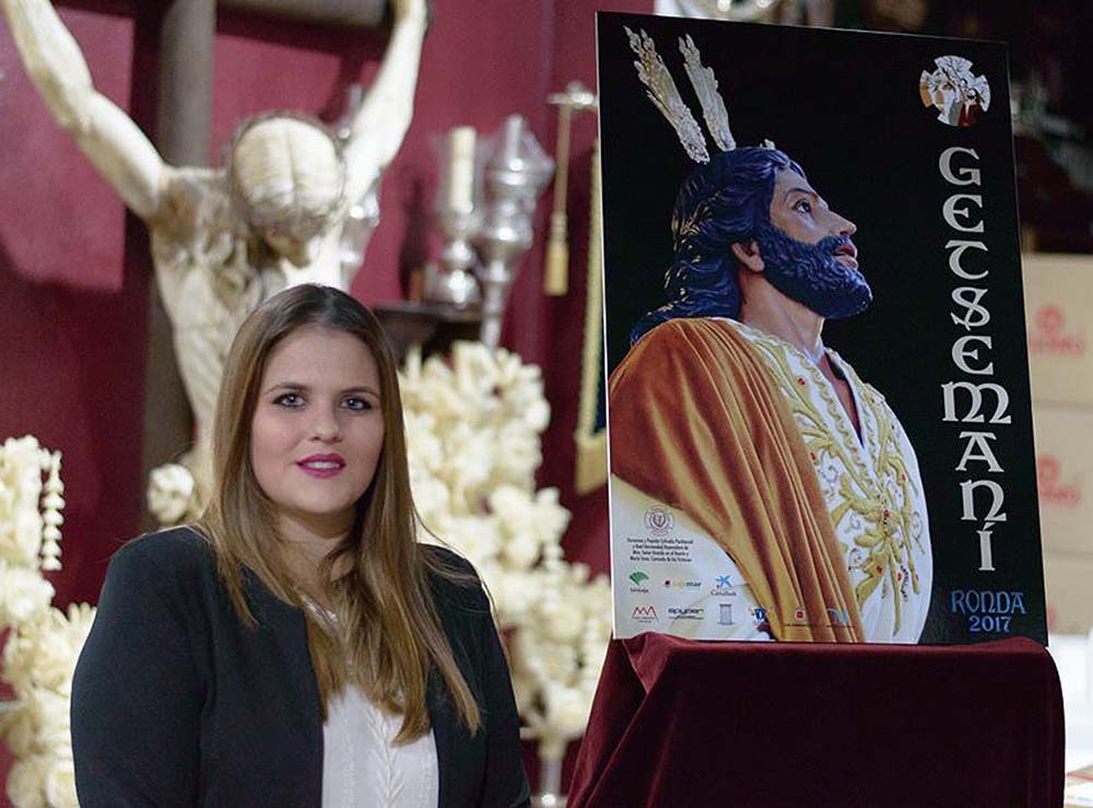 La autora junto al cartel que ha diseñado para este encuentro nacional de hermanos del Huerto. Foto Hermandad del Huerto.