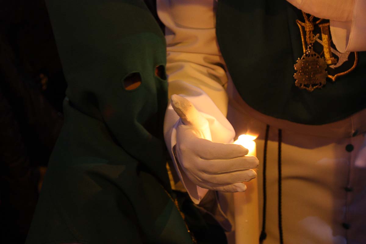 Un penitente intenta que se apague la vela de un pequeño nazareno de La Columna.