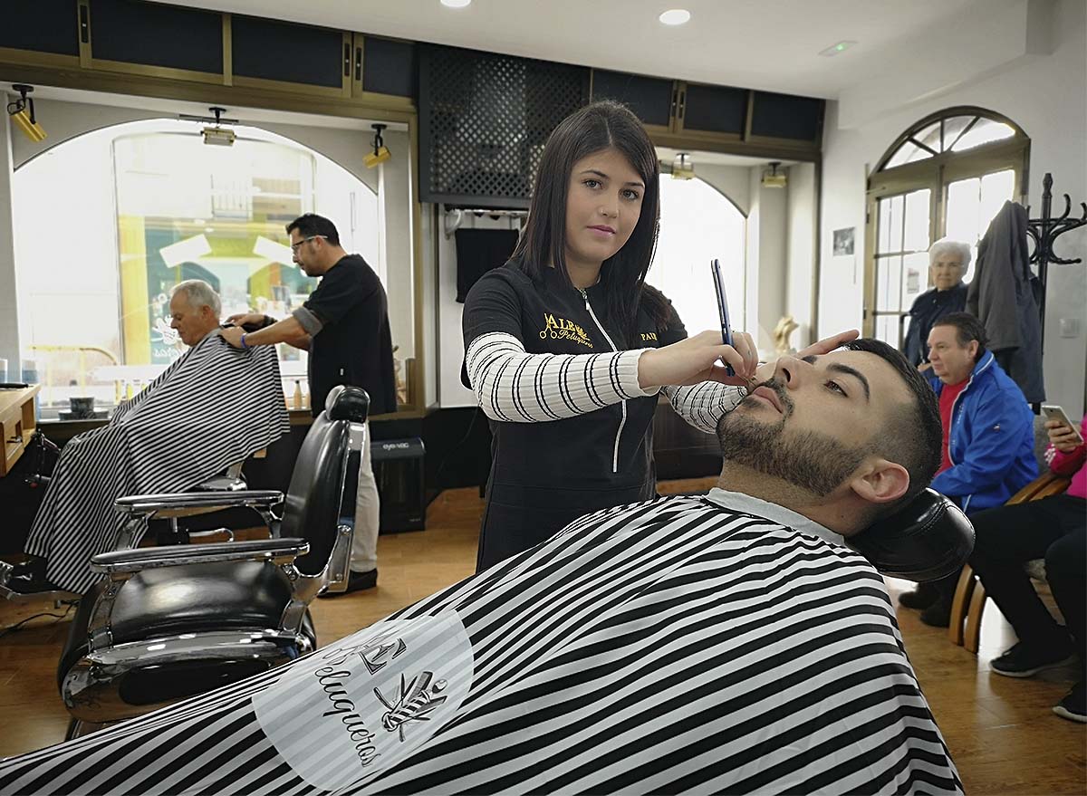 Paula recorta la barba a uno de su clientes en la peluquería masculina Ale.