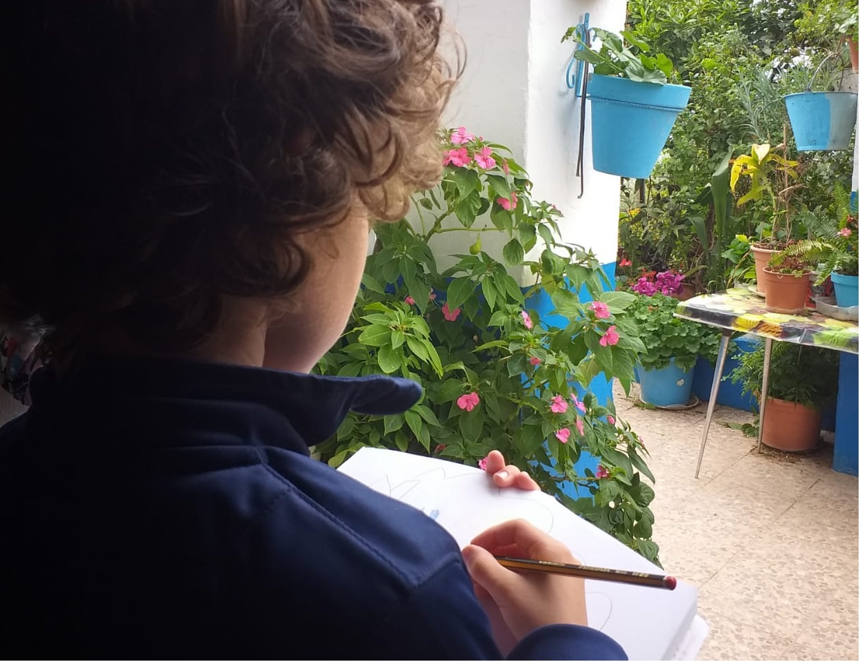 Un niño realiza un dibujo de Benalauría desde la terraza de su casa.