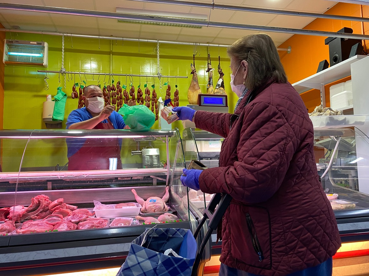 Una mujer compra en el mercado de abastos protegida con mascarilla y guantes.