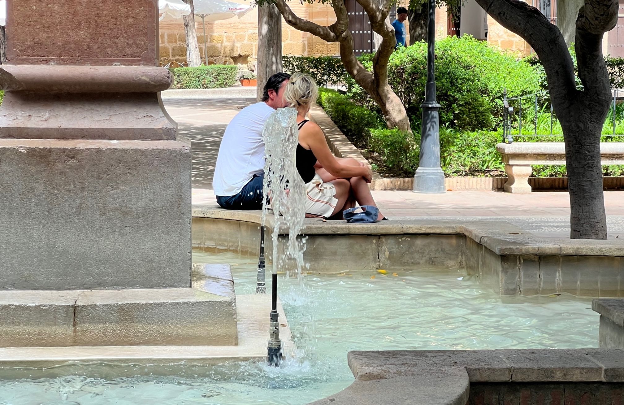 Dos turistas se refugian bajo una sombra y junto al agua.
