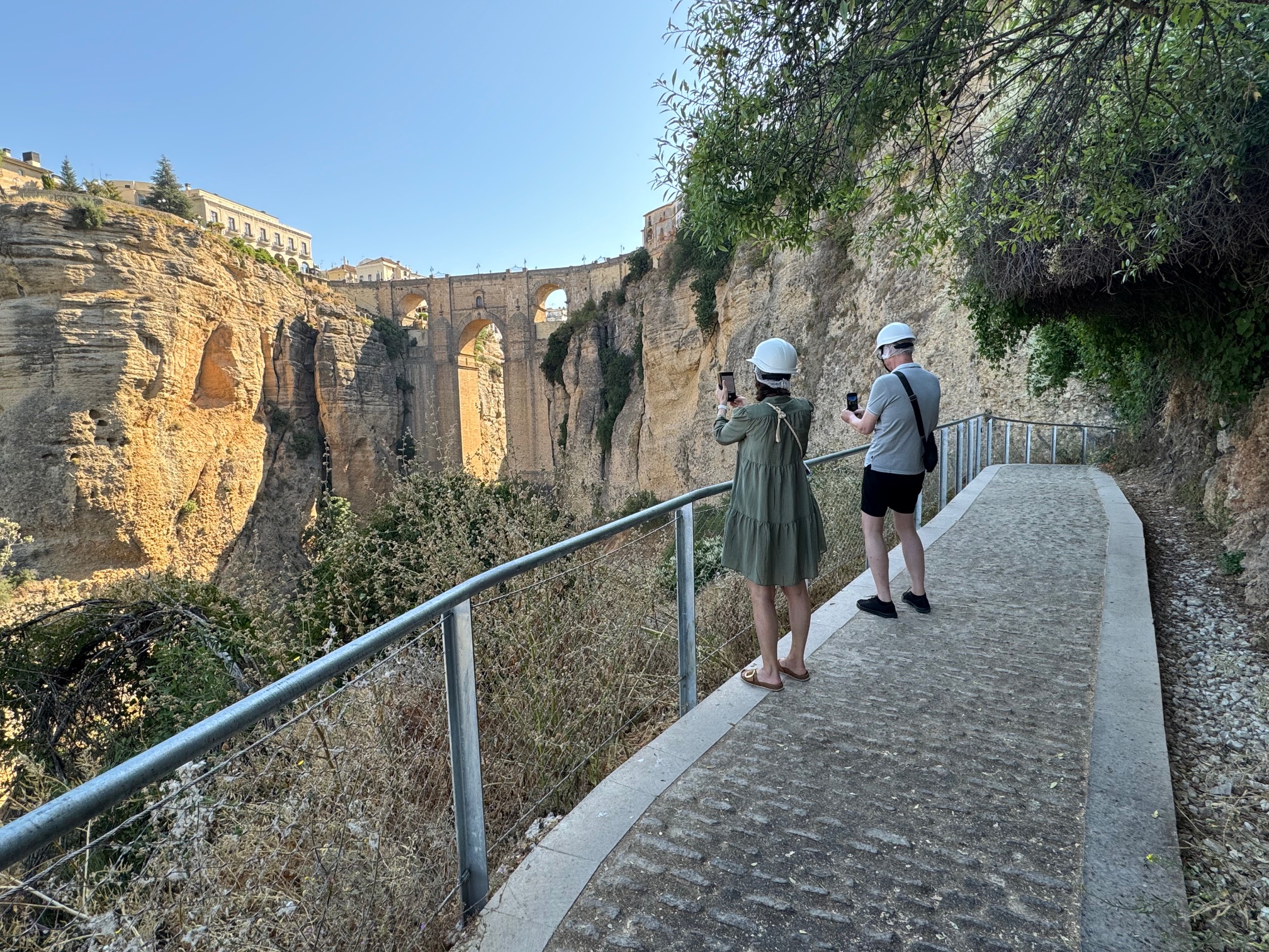 Dos turistas fotografían el Puente Nuevo desde el Camino del Desfiladero.
