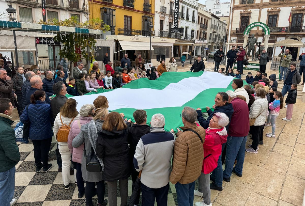 Autoridades, personas mayores y escolares han desplegado una gran bandera andaluza.