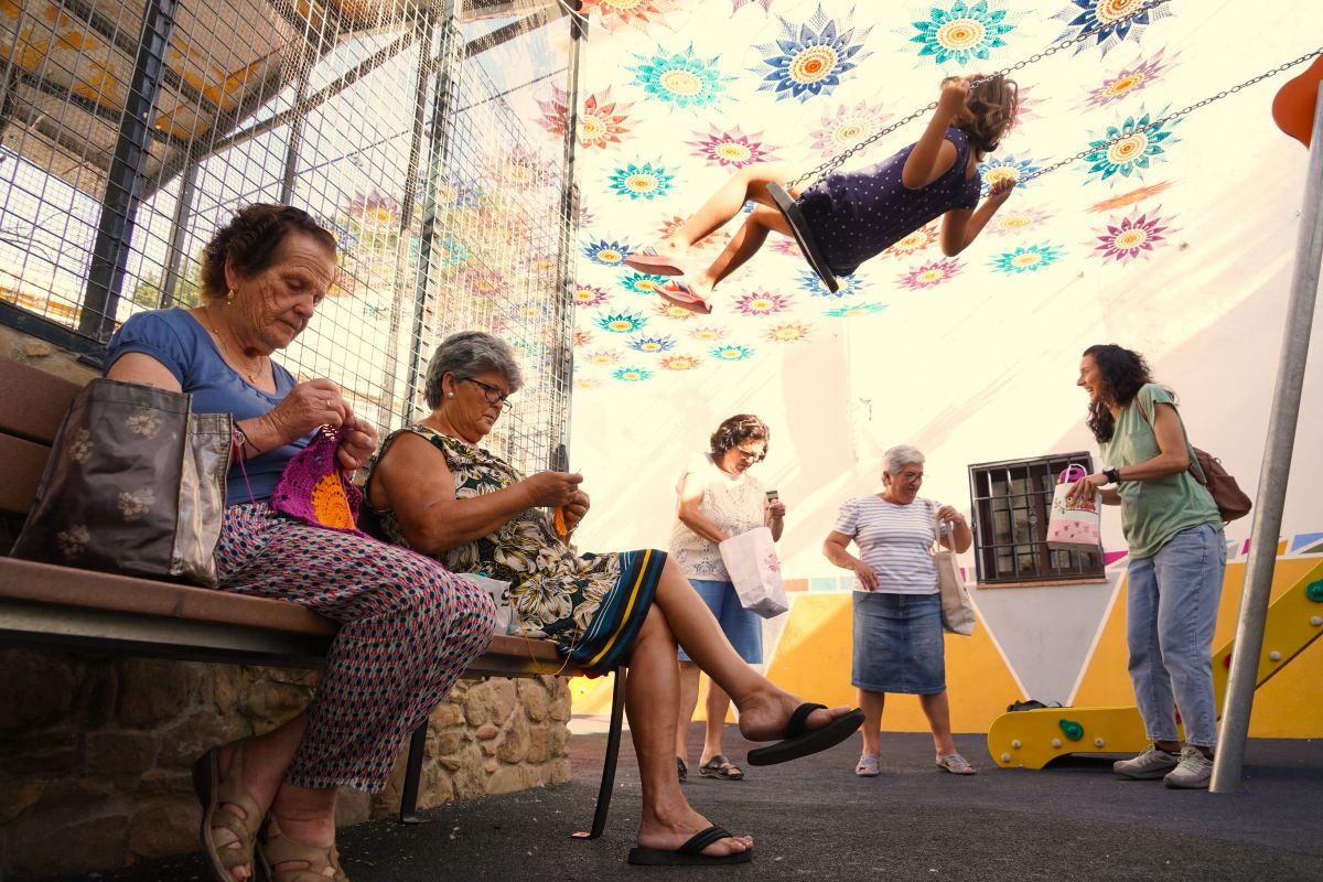 Las vecinas tejen el toldo de croche mientras una niña juega a su sombra.