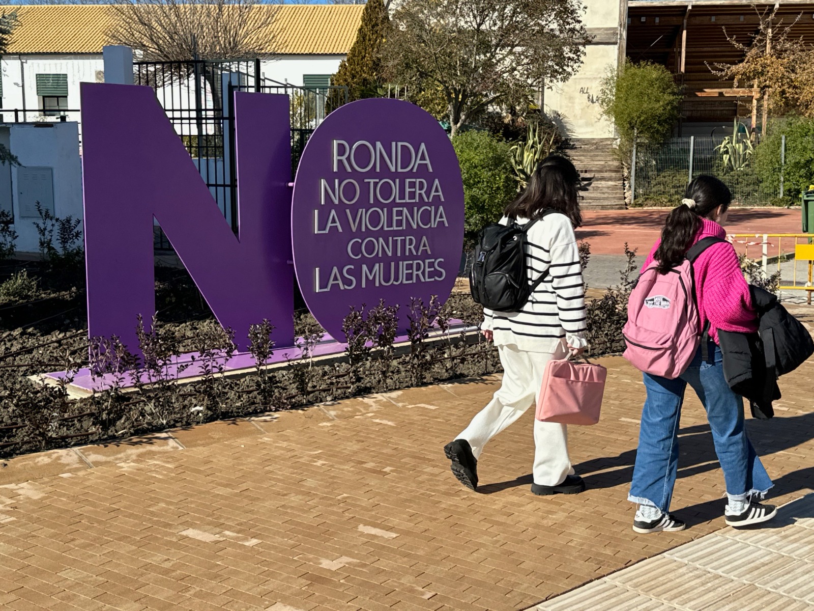 Dos jóvenes caminan junto a un letrero con el mensaje Ronda no tolera la violencia contra las mujeres.